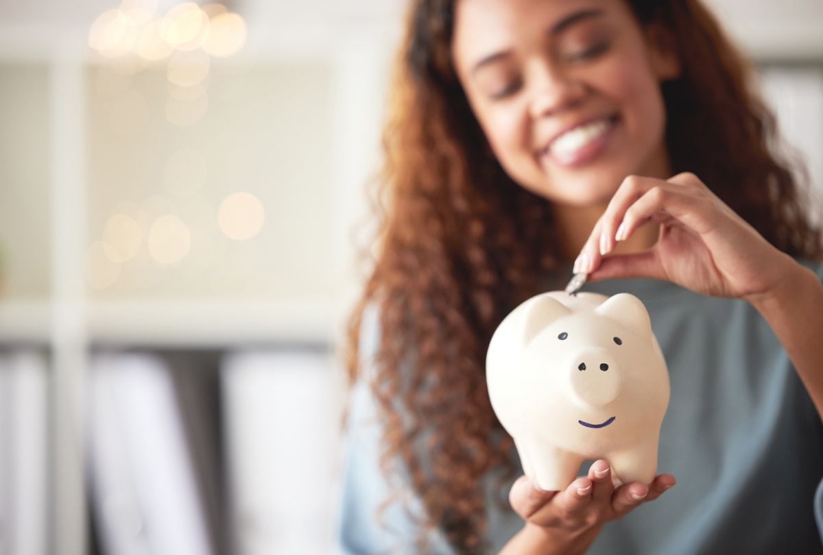 A young woman holding a piggybank and depositing a coin toward her savings