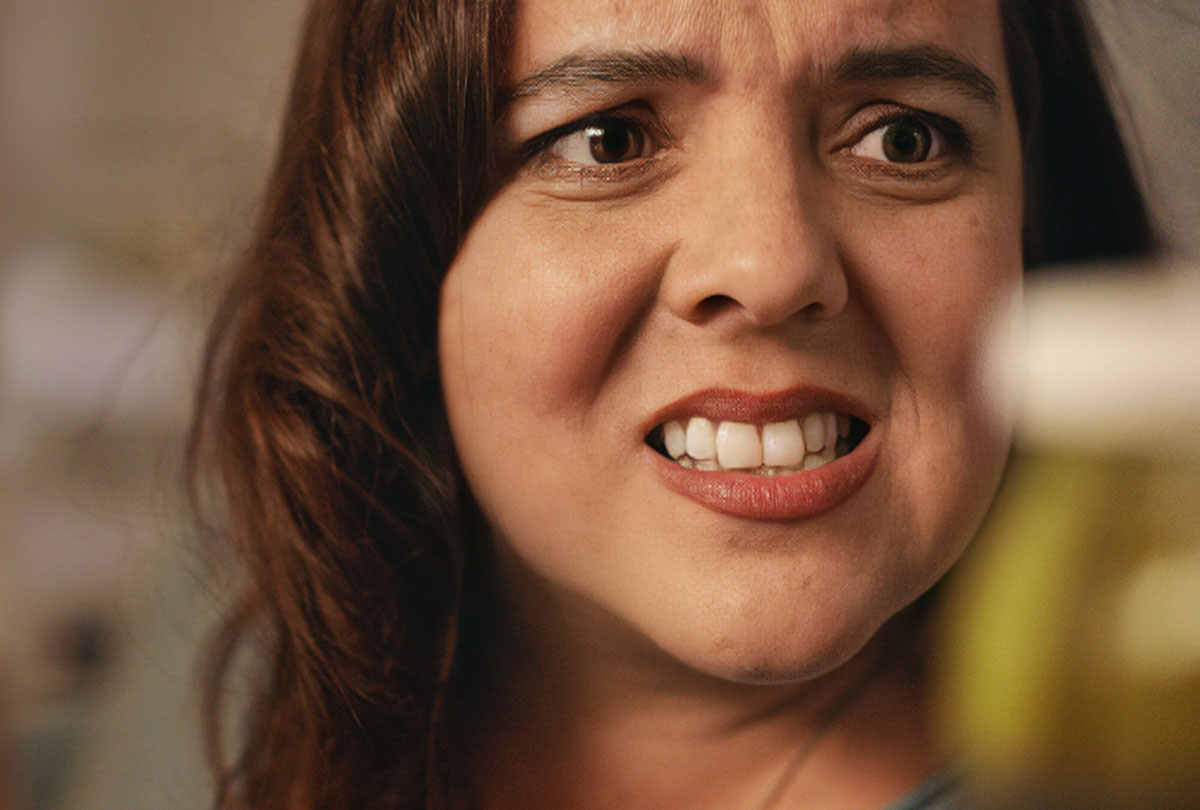 This image of a woman looking uncomfortable as she reaches for an item in the fridge while her friends talk about investing is part of the BCSC's public awareness campaign that talks about the lengths people may go to to avoid investing conversations.